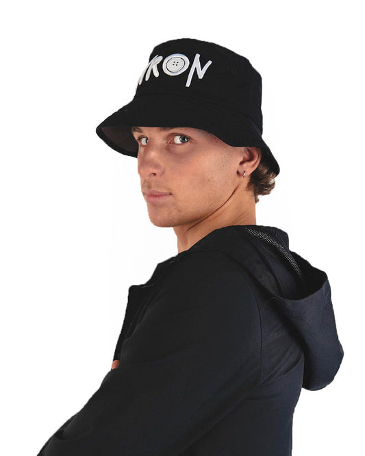 Profile shot of a model in black bucket hat with 'BYRON' logo, styled with a hoodie for an effortless coastal streetwear look.


