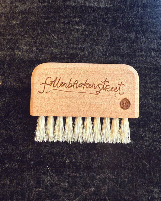 Close-up of FallenBROKENstreet wooden hat brush with logo branding burnt into the wood, showing fine bristle detail. Perfect compact accessory for cleaning and maintaining hats in timeless style.