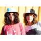 Close-up of two models wearing the FlipSide Bucket Hat – Black/White Reversible. One model wears the black side, the other the white side. Cotton canvas reversible bucket hat with wide brim, festival-ready design, and lightweight packable construction. Styled with casual streetwear in natural sunlight.