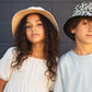 Two children wearing hats against a gray wall