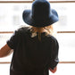 Model wearing The Janis Felt Hat – Navy, relaxed against a window, embodying effortless bohemian style.