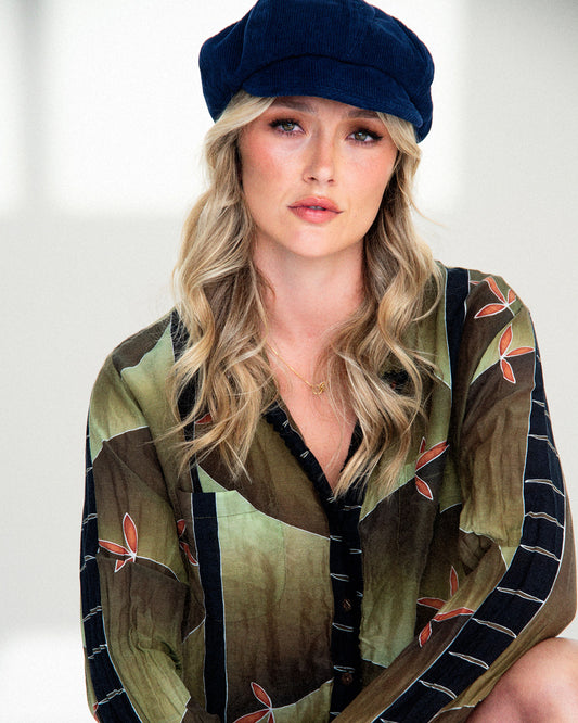 Woman wearing a patterned shirt and navy cap against a white background