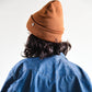 Back view of The Lucks Beanie in brown by FallenBROKENstreet. Wool blend ribbed knit design with fold cuff shown on model. The beanie’s snug yet flexible fit highlights its versatility, designed for both men and women as a seasonal essential for cooler days and nights.