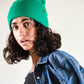Model wearing The Lucks Beanie in green, styled with a denim jacket. FallenBROKENstreet wool blend beanie with ribbed knit pattern and folded cuff. Signature logo badge detail adds subtle branding. Designed for warmth, comfort, and unisex styling, this beanie offers a versatile fit for both city streets and festival nights.