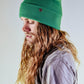 Lifestyle image of The Lucks Beanie in green, shown as the model adjusts the fit. Wool blend ribbed knit design with folded cuff and subtle logo badge. A versatile and warm unisex beanie from FallenBROKENstreet, designed to add effortless street style and practical comfort to everyday outfits.