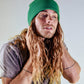 Side profile shot of The Lucks Beanie in green by FallenBROKENstreet. Wool blend ribbed knit design with folded cuff and logo patch shown on model. A cosy, unisex accessory made for cooler weather, perfect for streetwear layering, festivals, and everyday use across all seasons.