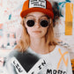 Model wearing red Marty Baptist cap with sunglasses and printed tee in art-covered room.