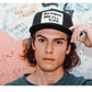Model wearing Strum Cap with hand near face and colourful graffiti background.