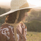Young girl wears The Lover Straw Hat in natural straw, shown from the side against a warm afternoon light. Ideal for nature play, picnics, and long beach days.


