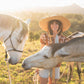 Children walk through a field with a white horse, one wearing The Lover Straw Hat. The scene captures the spirit of exploration and timeless summer style.


