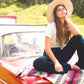 Woman in The Wanderer hat sitting on a classic car with blanket, styled in a casual road trip look – Fallenbrokenstreet.