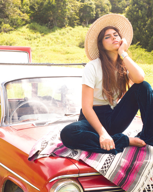 Woman in The Wanderer hat sitting on a classic car with blanket, styled in a casual road trip look – Fallenbrokenstreet.