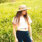 Woman wearing The Wanderer straw hat in a grassy field, styled with a white tee and navy pants – Fallenbrokenstreet.