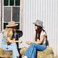 Two Women drinking wine wearing vintage Western cowgirl hats with cowboy boots on haybales