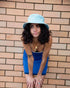 Model wearing Saturday Bucket Hat – Blue by FallenBROKENstreet. Cotton chenille bucket hat with wide brim, cotton inner band, and UPF 50+ sun protection. Styled in a blue slip dress, highlighting casual summer elegance.
