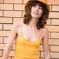 Model wearing Saturday Bucket Hat – Tangerine, photographed outdoors against a brick wall. Cotton chenille wide brim hat with UPF 50+ sun protection, lightweight and breathable design, styled with a yellow dress for a bold, playful summer look.