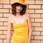 Portrait of model wearing the Saturday Bucket Hat – Tangerine. Wide brim cotton chenille summer hat with UPF 50+ rating, breathable inner band, and travel-ready durability. Styled with casual summer outfit against a brick wall.