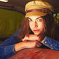 A women wears a fallen broken street fisherman cap while sitting in the back seat of a vintage car.