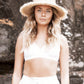 Model wearing The Seeker Straw Hat in a sunlit setting, styled with white boho separates, highlighting its wide brim and effortless silhouette.