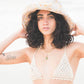 Close-up of model in Sunday Bucket Hat – Paisley by FallenBROKENstreet. Cotton canvas bucket hat with breathable band and wide brim, designed for festivals, beaches, and everyday wear. Styled in neutral swimwear, photographed outdoors at the seaside, showcasing the hat’s lightweight and playful patterned finish.