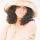Model wearing the Sunday Bucket Hat – Paisley by FallenBROKENstreet. Cotton canvas summer hat with wide brim for shade and a cotton inner band for comfort. Features all-over paisley design, styled in minimal swimwear against a soft beach backdrop. A relaxed unisex bucket hat built for summer adventure.