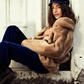 Woman wearing a fur coat and navy outfit sitting against a wall.