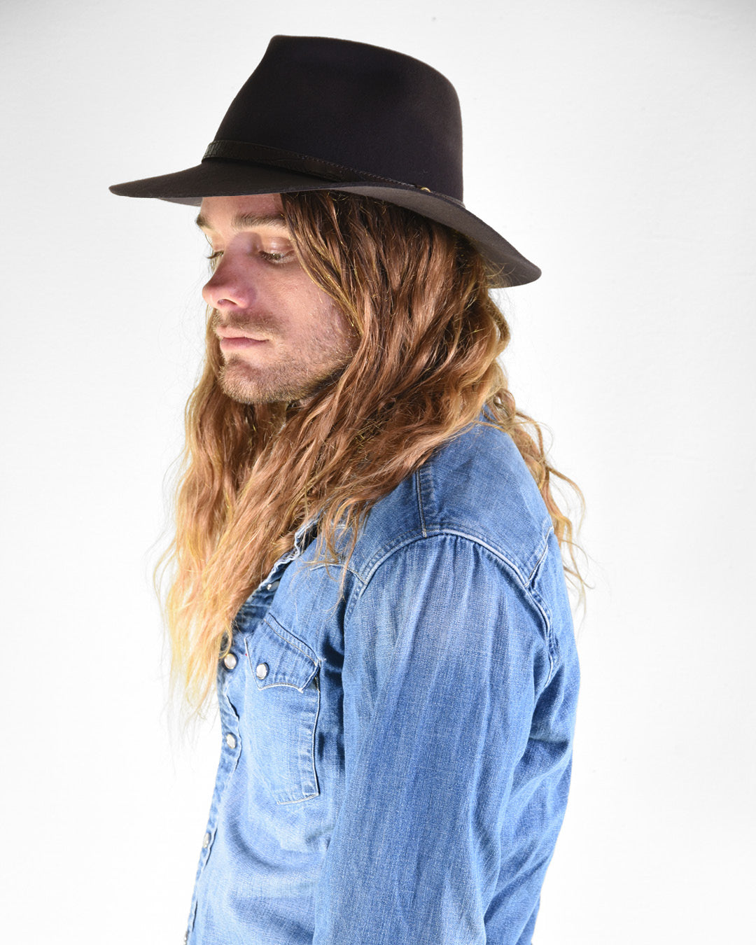 Man wearing a black hat and blue denim shirt against a white background