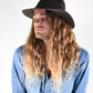 Man with long hair wearing a black hat and blue denim shirt on a white background
