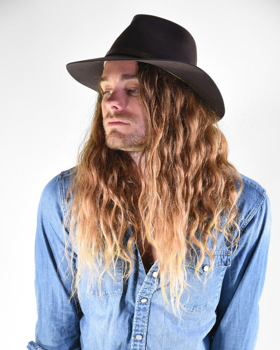 Man with long hair wearing a black hat and blue denim shirt on a white background