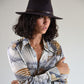 Woman wearing a patterned shirt and black hat against a plain background