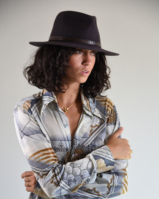 Woman wearing a patterned shirt and black hat against a plain background
