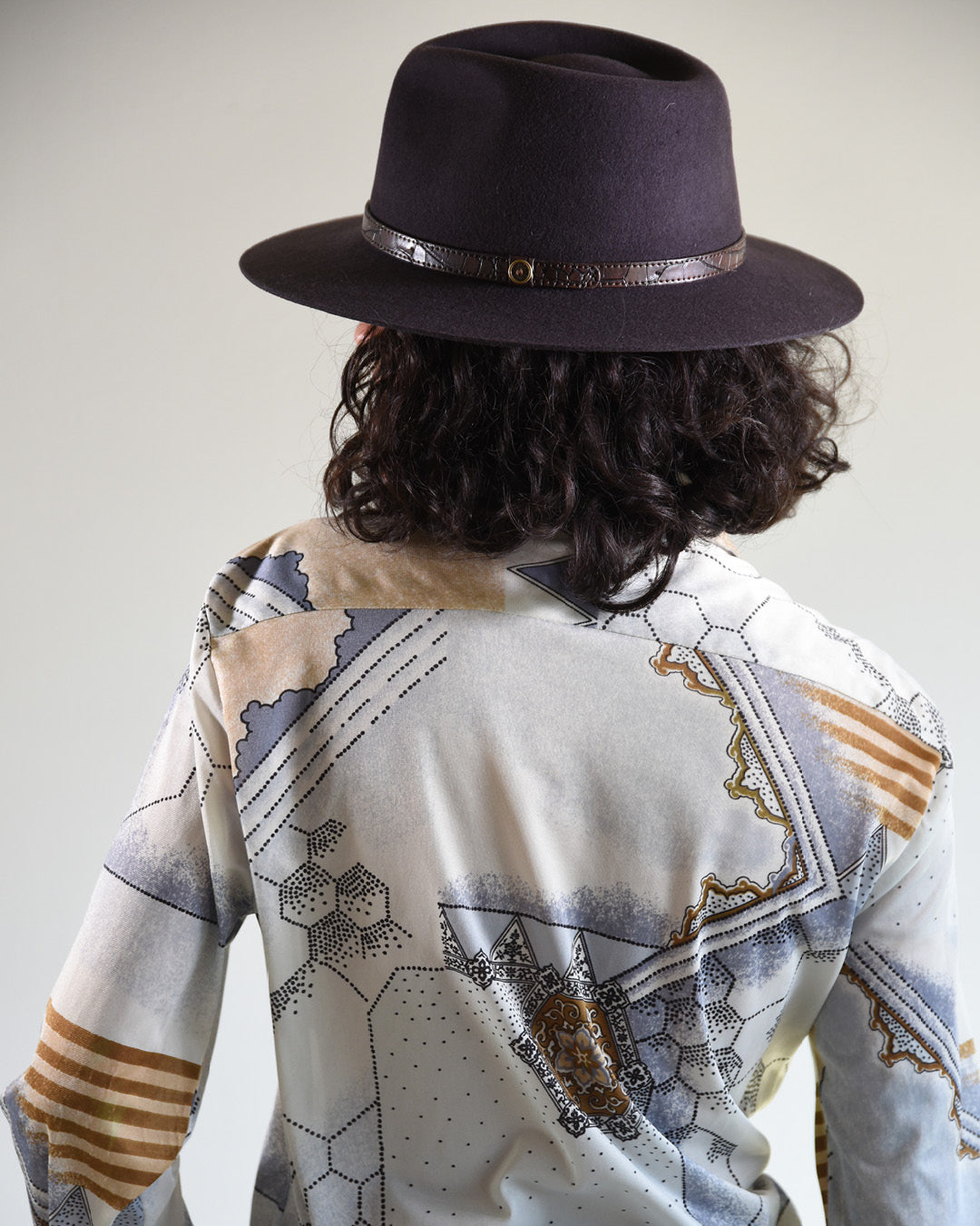 Person wearing a dark hat and patterned shirt with a plain background
