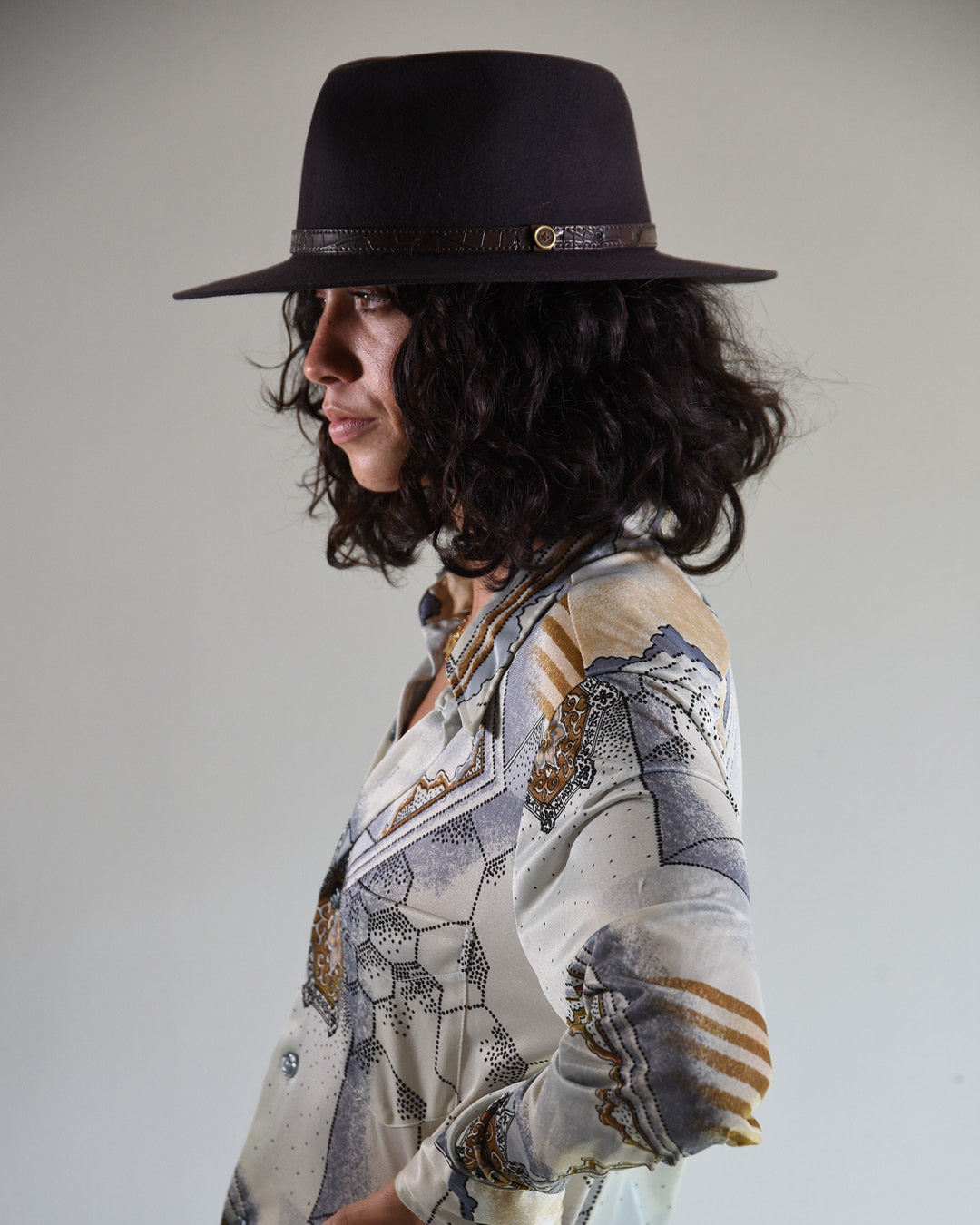 Woman wearing a patterned shirt and black hat against a plain background