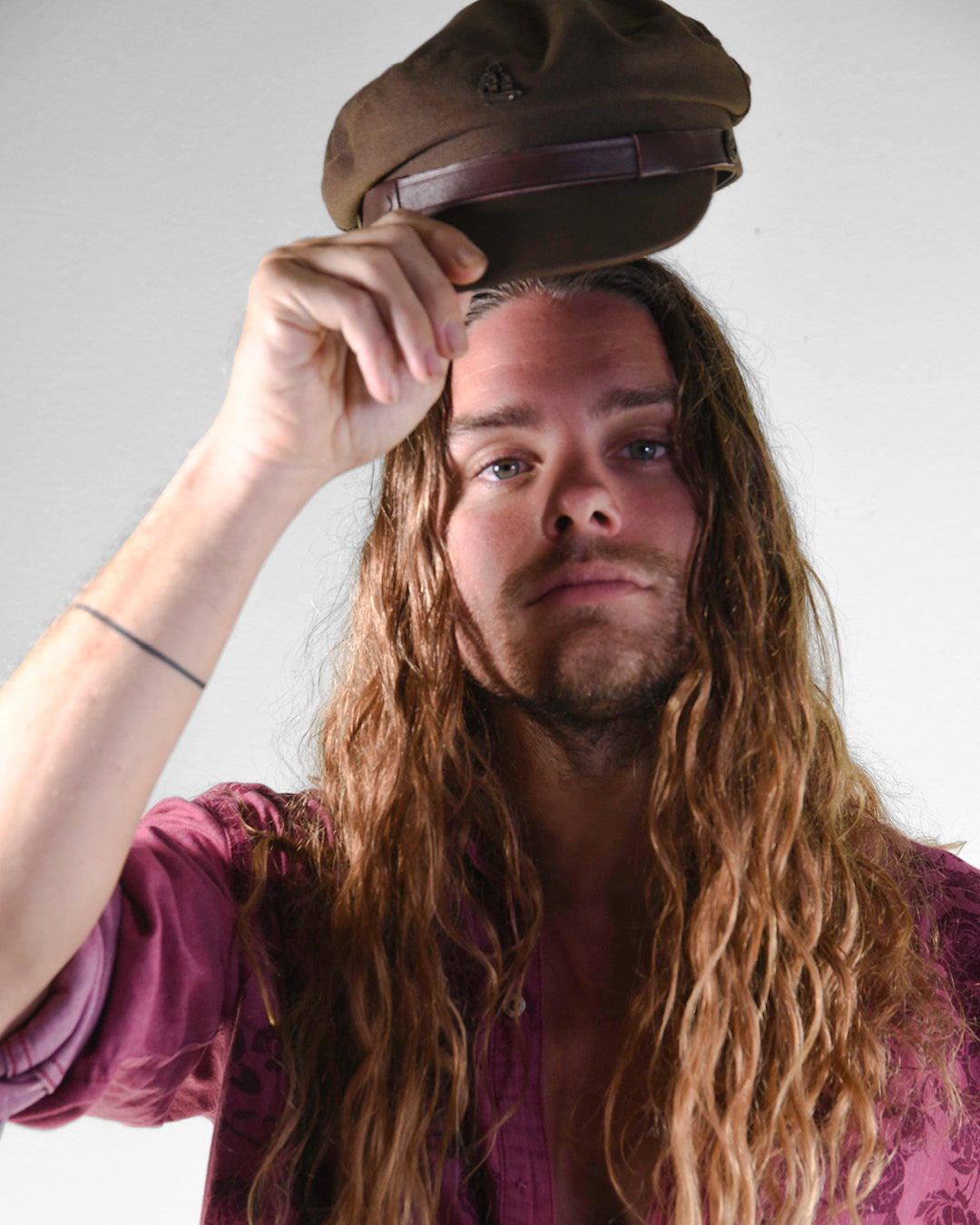 Man with long hair wearing a brown cap against a plain background
