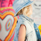 Child wearing a denim hat and vest in front of a colorful abstract background