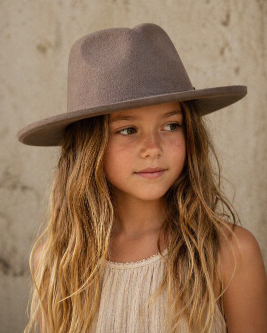 Young girl wearing a brown hat against a neutral background