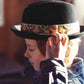 Person wearing a black fedora with a patterned band, adjusting it.