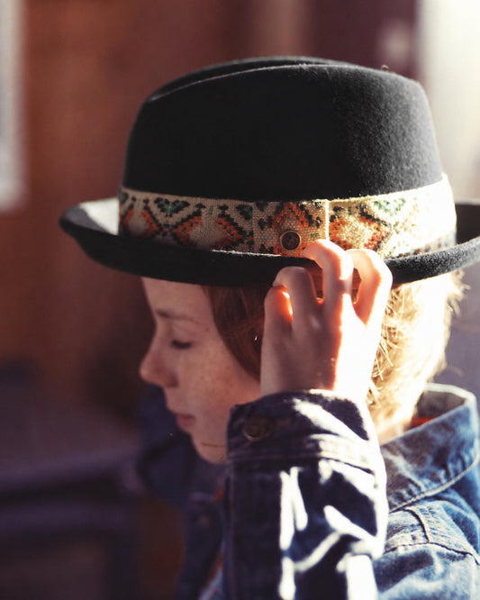 Person wearing a black fedora with a patterned band, adjusting it.