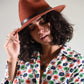 Woman wearing a brown fedora hat and a colorful floral shirt against a plain background