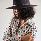 Person wearing a dark hat and a colorful floral shirt against a plain background