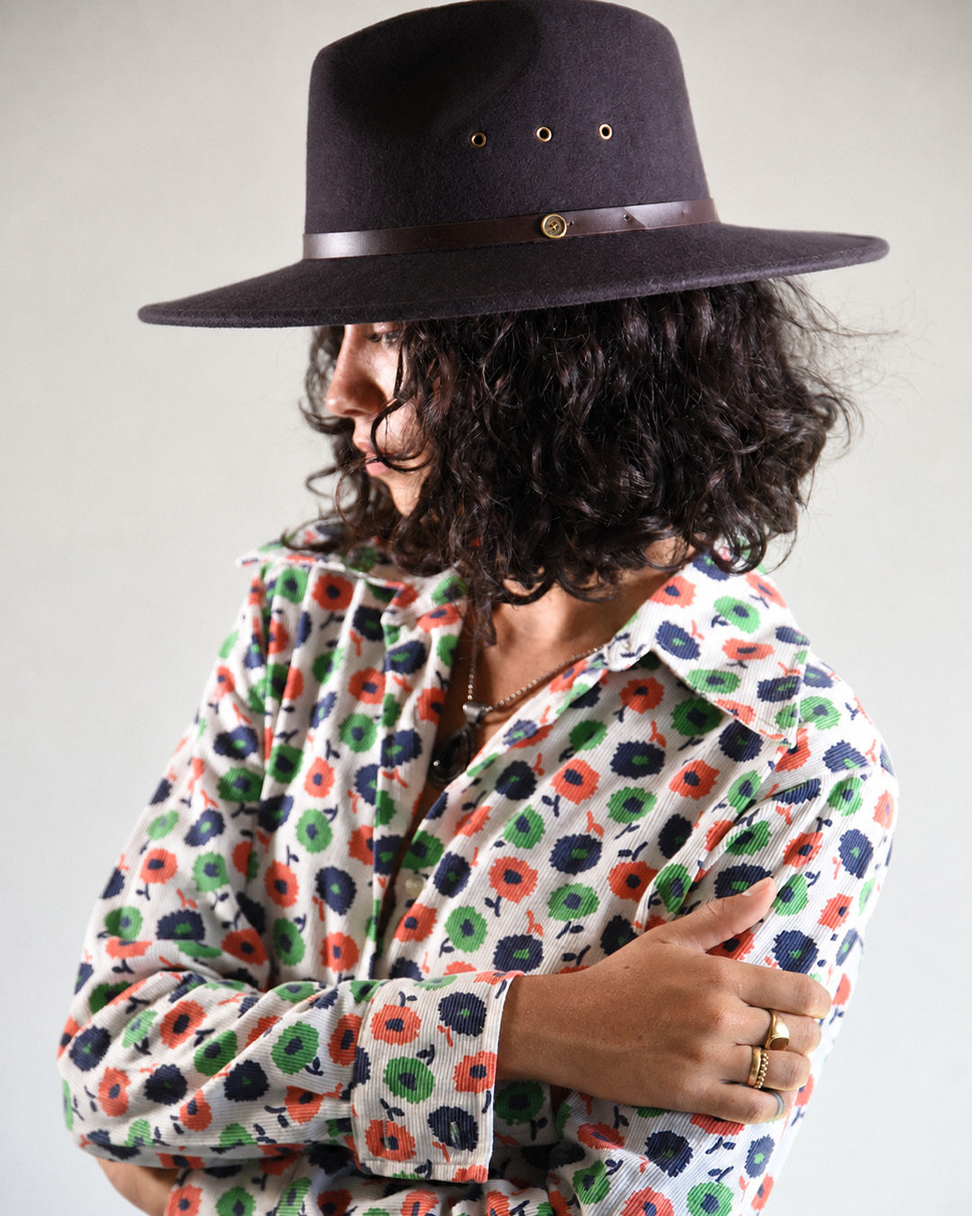 Person wearing a dark hat and a colorful floral shirt against a plain background