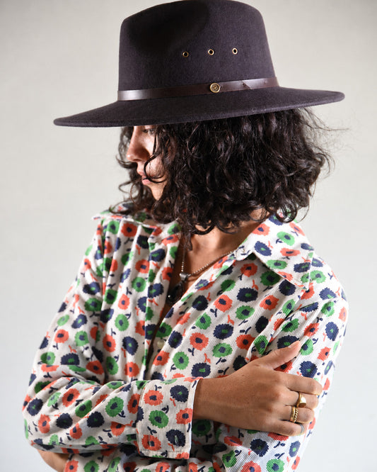 Person wearing a dark hat and a colorful floral shirt against a plain background