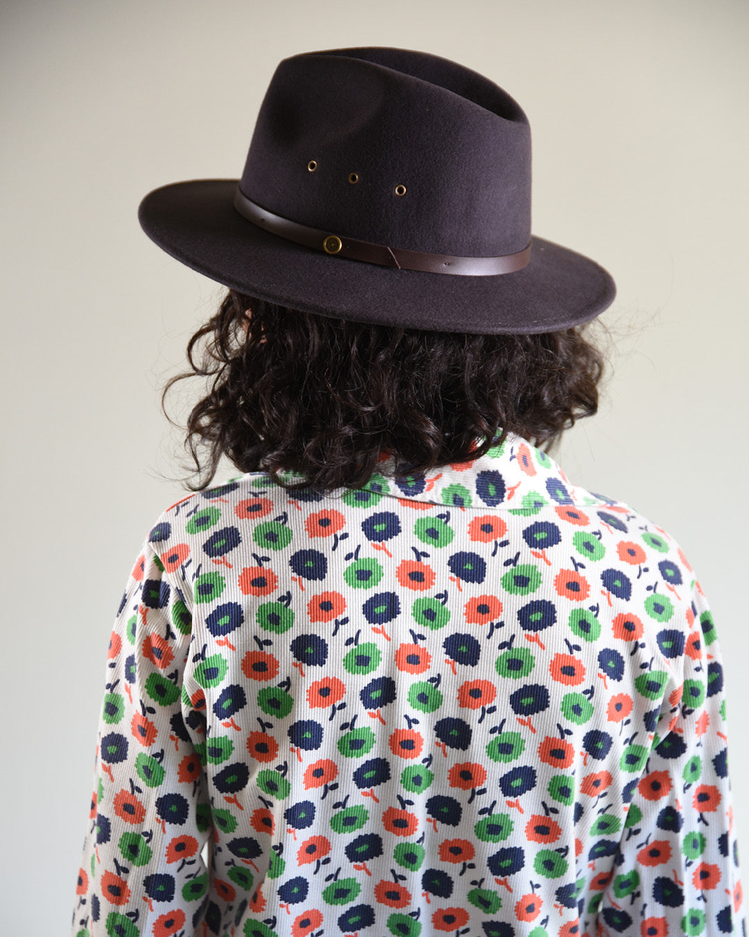 Person wearing a dark hat and a floral patterned shirt against a plain background