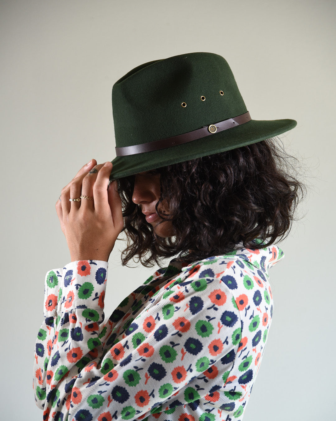 Person wearing a green fedora hat with a brown band against a plain background