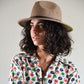 Woman wearing a floral blouse and a brown hat against a plain background