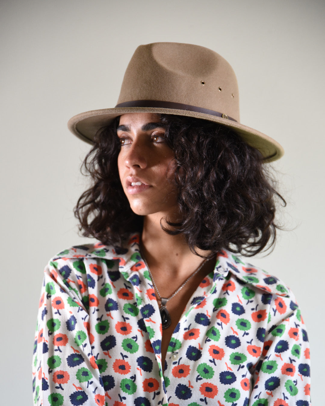 Woman wearing a floral blouse and a brown hat against a plain background