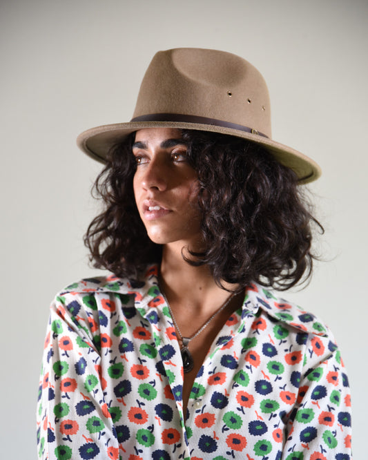 Woman wearing a floral blouse and a brown hat against a plain background
