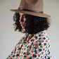 Person wearing a brown hat and a floral patterned shirt against a plain background