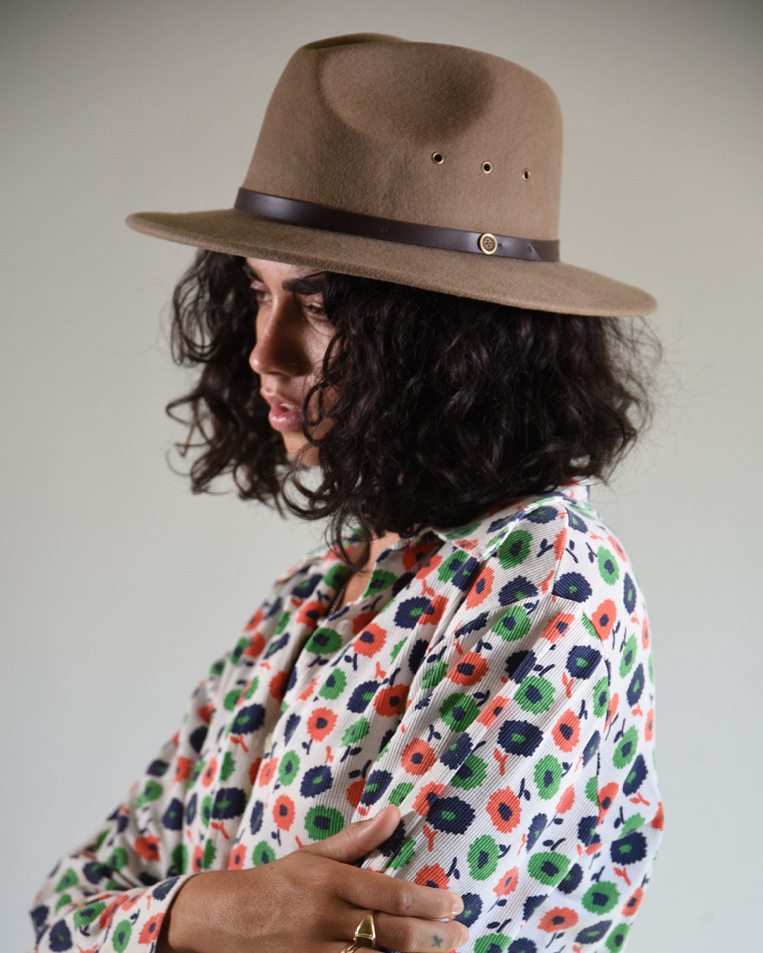 Person wearing a brown hat and a floral patterned shirt against a plain background