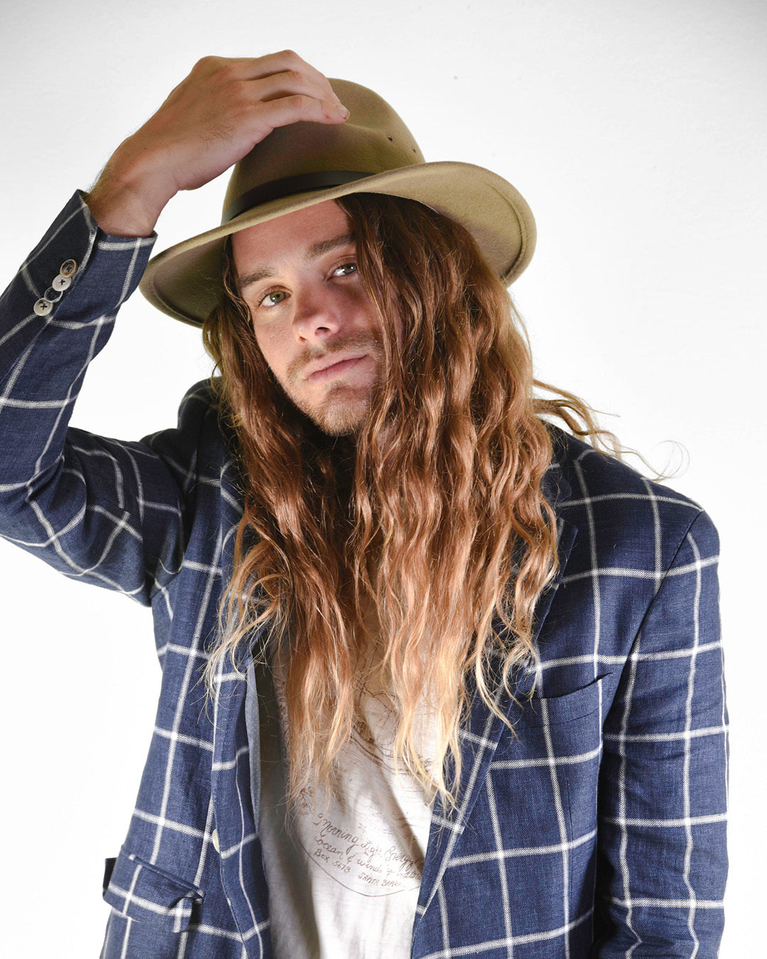 Man wearing a blue checkered blazer and beige hat against a white background